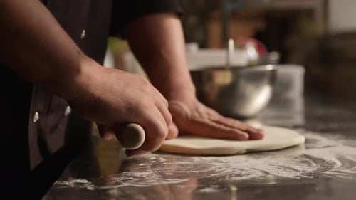 The dough rolling the man's hands on counter top with flour. Preparation of the dough