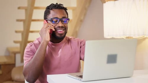 Man Using Laptop Talking on Smartphone