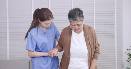 Young Woman Helping Senior Woman Walk Indoors