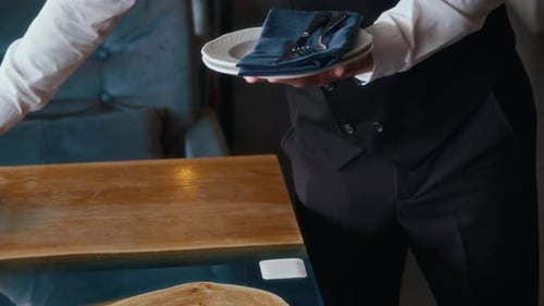 Unrecognizable Waiter Serving Plates and Cutlery on Table in Restaurant