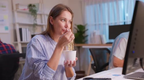 Caucasian businesswoman eatting noodles while work in office at night.