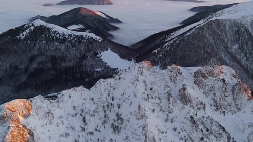 Snowy Rocky Peaks Illuminated By Sunset Light with Fog Draping Below in the ValleyAerial View