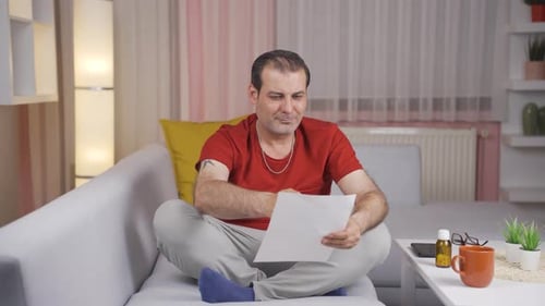 Man Reads a Document at Home on Couch