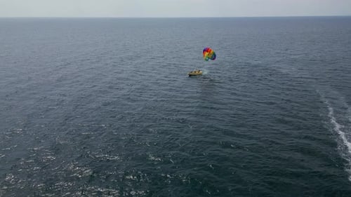 Drohnenvideo eines farbenfrohen Parasailers, das über dem offenen Meer schwebt und von einem Schnellboot unter der Antenne gezogen wird