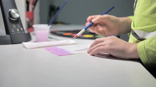 Boy Paints with a Brush and Pink Paint While Sitting at a White Table at Home