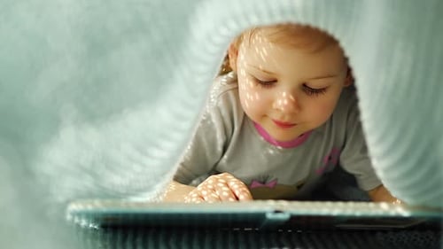 Little Girl Enjoying of Review a Book Under Blue Knitted Plaid in Sunny Morning