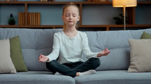 Méditation calme caucasienne pour enfant fille à la maison en position du lotus sur canapé, méditant pour petite fille