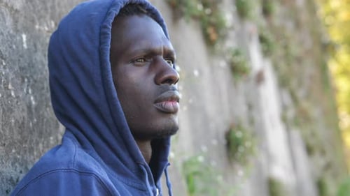 entmutigter junger Migrant mit Kapuze hebt den Kopf und schaut auf