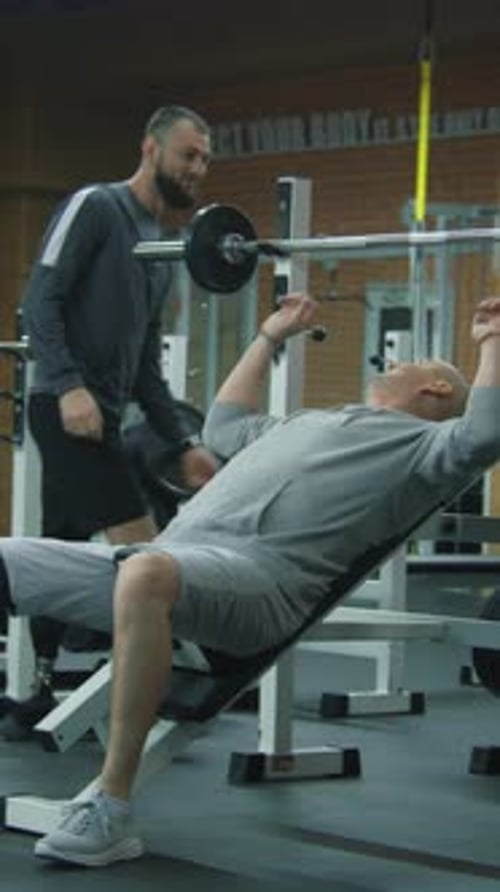Athletic Man with Prosthetic Leg Exercises with Barbell in Gym with Personal Coach