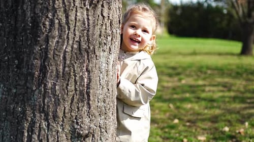 Garotinha feliz se escondendo atrás de uma árvore no parque da primavera em Praga, Europa