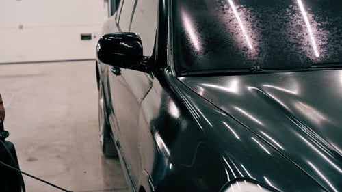 close-up A male car wash employee applies car wash detergent to a black luxury car using spray gun