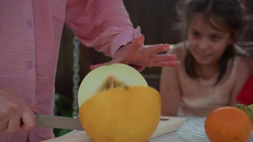 Frau schneidet Obst Frau schneidet Melone draußen Mädchen sieht Frau beim Schneiden reifer Melonen Mutter zu