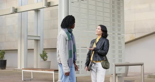 Diverse friends talking in plaza with woman gesturing to start chat, picking up skateboard, walking
