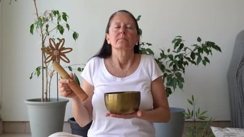 Woman Sits Calmly With Eyes Closed, Holding Tibetan Singing Bowl And Mallet While Breathing. Sound