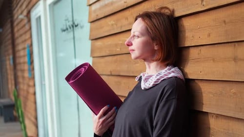 Woman Holding Yoga Mat by Wooden Wall
