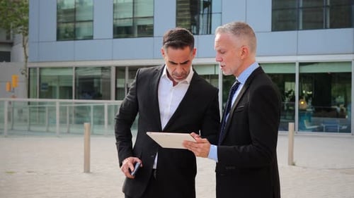 Two Confident Businessmen Discussing Important Project Details While Examining Data on a Tablet in a