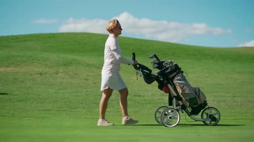 A Woman Walks on a Golf Course and Pulls a Cart with Golf Equipment