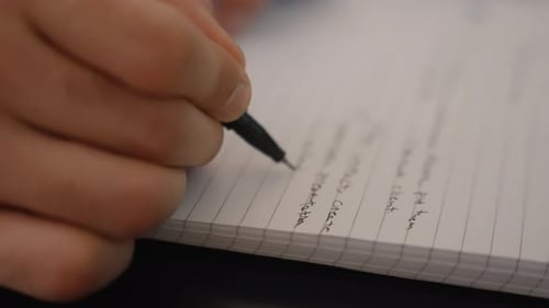 Extreme close up of a man writing on a notebook with a black pen