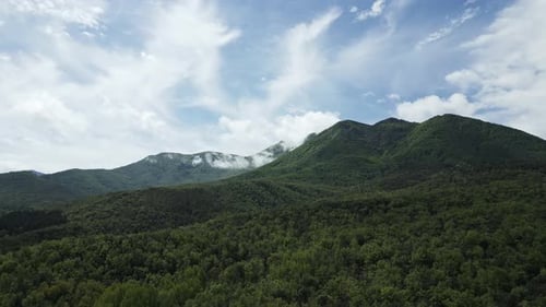 Green mountain peaks touching white clouds on sunny day