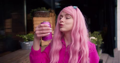 Una chica vestida de rosa y con cabello rosado bebe refresco de una lata rosa en la calle Color rosa