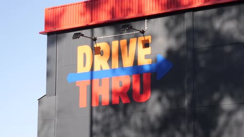 Orange-painted "DRIVE THRU" signage painted on a building's wall in gray and arrow pointing towards