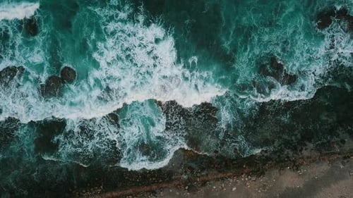 Aerial View Of Turquoise Ocean Waves Crashing Against A Rocky Shoreline