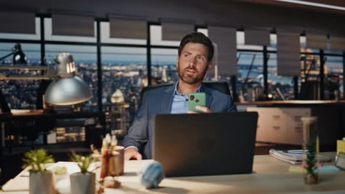Man Using Phone at Desk in Modern Office at Night