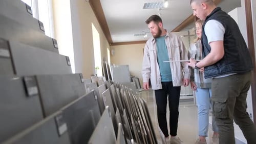 A Young Couple with a Salesman Chooses a Large Ceramic Tile for Floor Repair