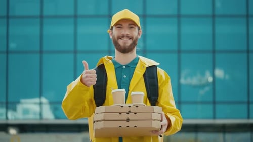Porträt eines gutaussehenden Lebensmittellieferanten in Uniform, der Pizza- und Kaffeekartons hält