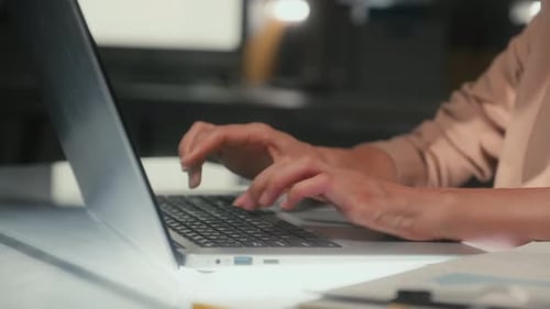 Hände einer Mitarbeiterin, die spät im Büro E-Mail-Texte auf dem Laptop tippt