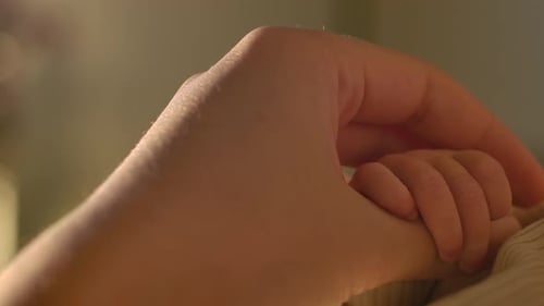 Newborn's Delicate Hand Grasping Mother's Thumb. closeup shot