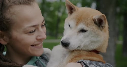 Smiling Woman Holds Shiba Inu Dog Outdoors