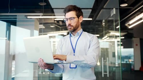 IT engineer admin works on a laptop while standing in business office of data center.