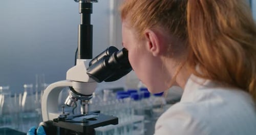 Female Scientist Sits and Works with Microscope in Bright Medical Laboratory