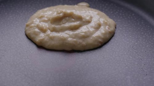 Close-up of pouring pancake batter on a hot pan.