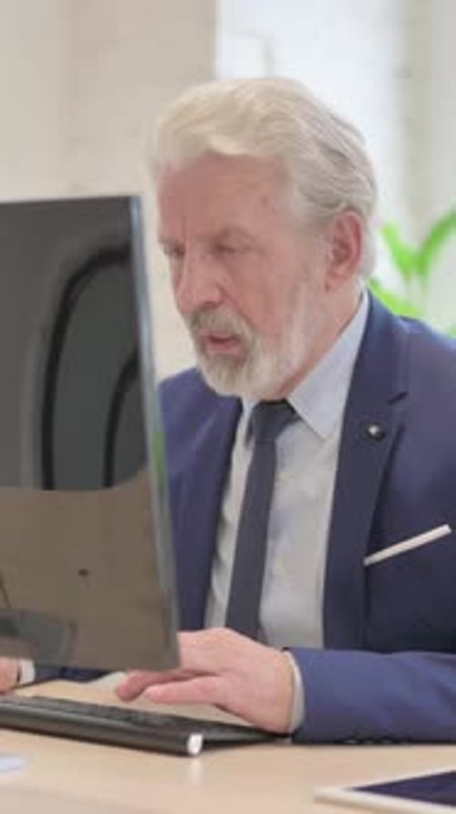 Senior Man Works at Computer in an Office