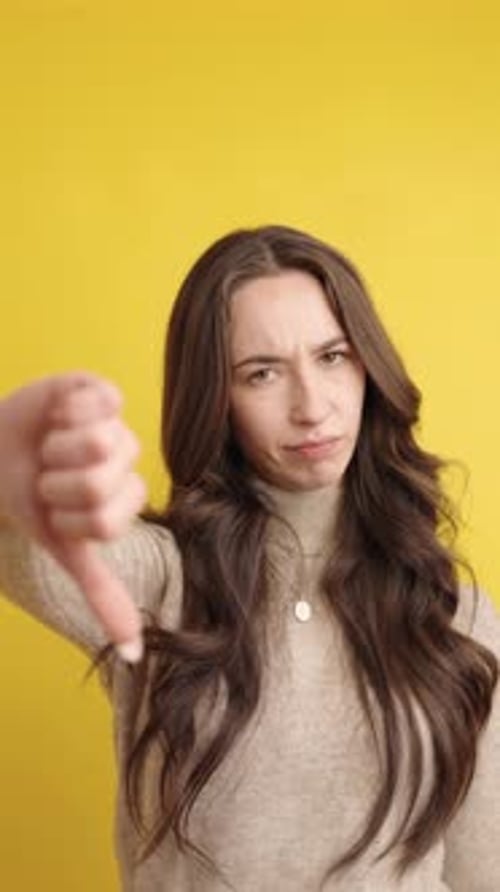 Young Woman Giving Thumbs Down Gesture on Yellow