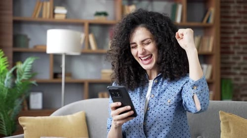 Excited Woman Cheering While Looking at Smartphone Indoors