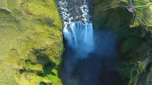 Skogafoss waterfall in the springtime. Vibrant green grass. Slow motion aerial view