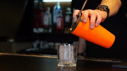 Barman Pouring Fresh Alcoholic Drink Into the Glasses with Ice Cube on the Bar Counter Cropped Slow