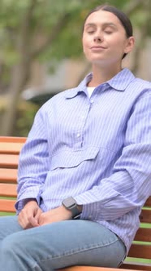 Woman Sits on Bench Checking Smartwatch in Park
