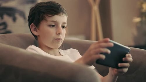Dark-Haired Child Plays With Tablet in Chair