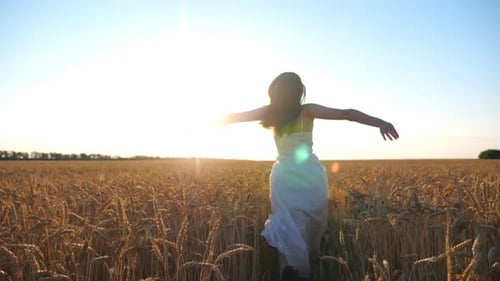 Carefree Woman Running Across Wheat Field with Outstretched Hands Happy Girl in White Dress Jogging