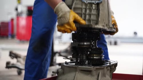 Mecânico de automóveis repara transmissão manual na garagem Técnico profissional em uniforme azul