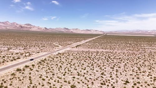 Drone following a car while rotating slightly driving on a long desert road in 4k