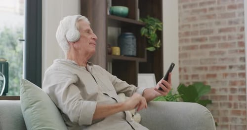 Mature Man Using Phone with Headphones Indoors