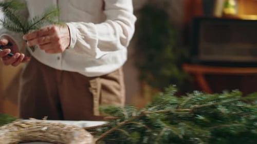 Unrecognizable Senior Woman Cutting Branch to Make Christmas Wreath Indoors at Home Advent