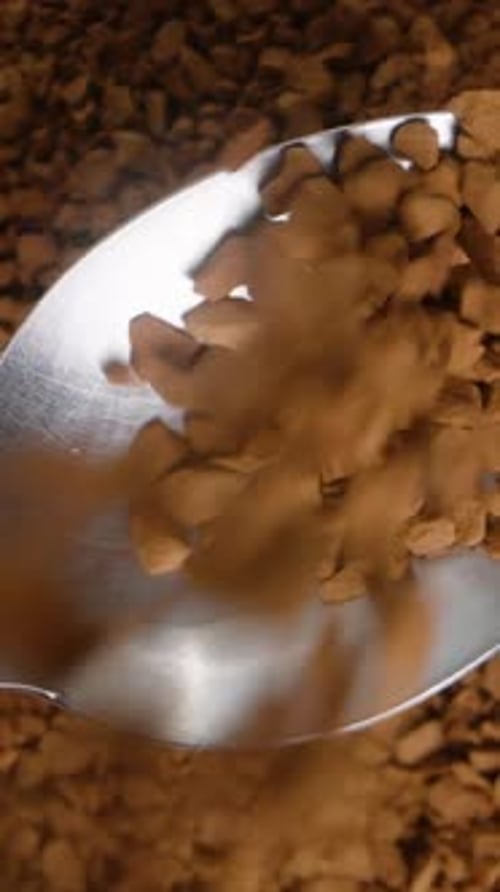 Vertical video. Rotating background of soluble coffee granules being poured into a spoon, top view.