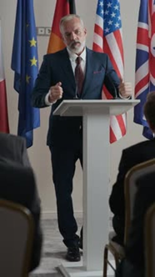 Man Giving Speech at Podium with Flags Behind