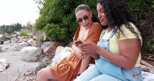 Happy Young Women Friends Talking and Using Smart Phone on Beach 2529 Years